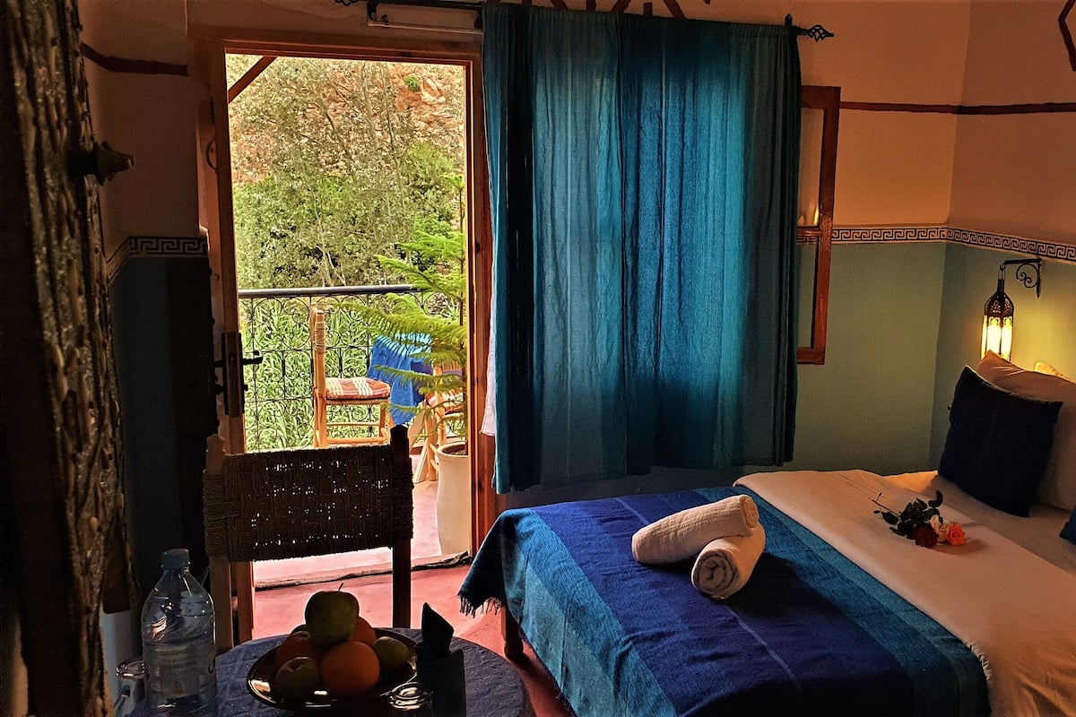 Ein Schlafzimmer mit Bett, Nachttisch, Wandlampe und Blick auf Grünflächen.