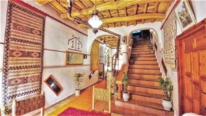 Un interior tradicional con una escalera de madera, paredes con diseños y plantas en macetas.