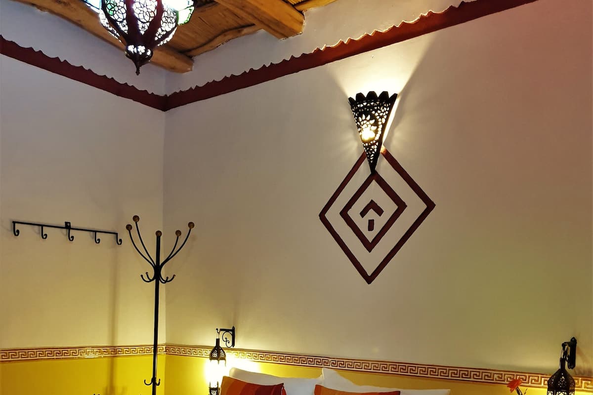 Ein Hotelzimmer mit einem Bett, einem Nachttisch mit Lampe, einem Wandhaken und einem dekorativen Wandbild.