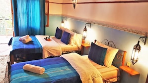 Habitación de hotel con dos camas, cada una con cubrecama azul y blanco, una mesita de noche con lámpara y una pared decorativa con patrón geométrico.