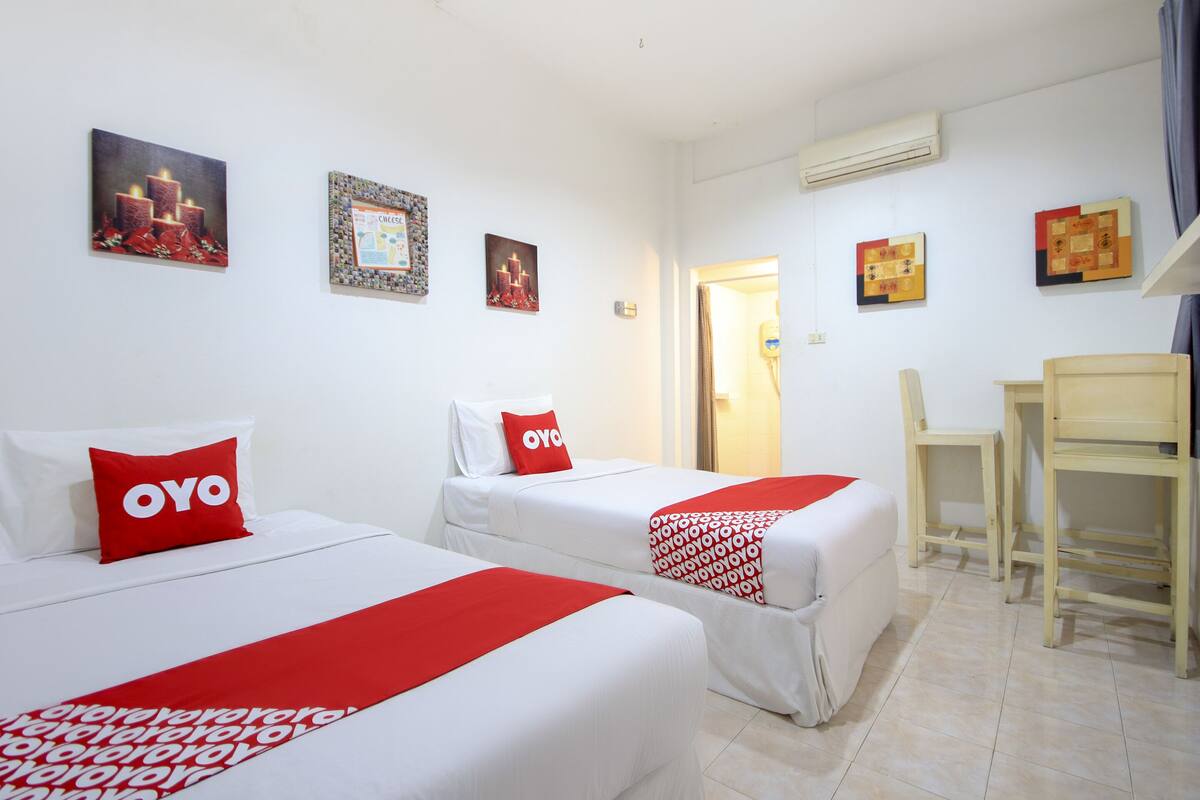 A hotel room with two beds, each with a red and white blanket and pillows, and a small desk with a chair.