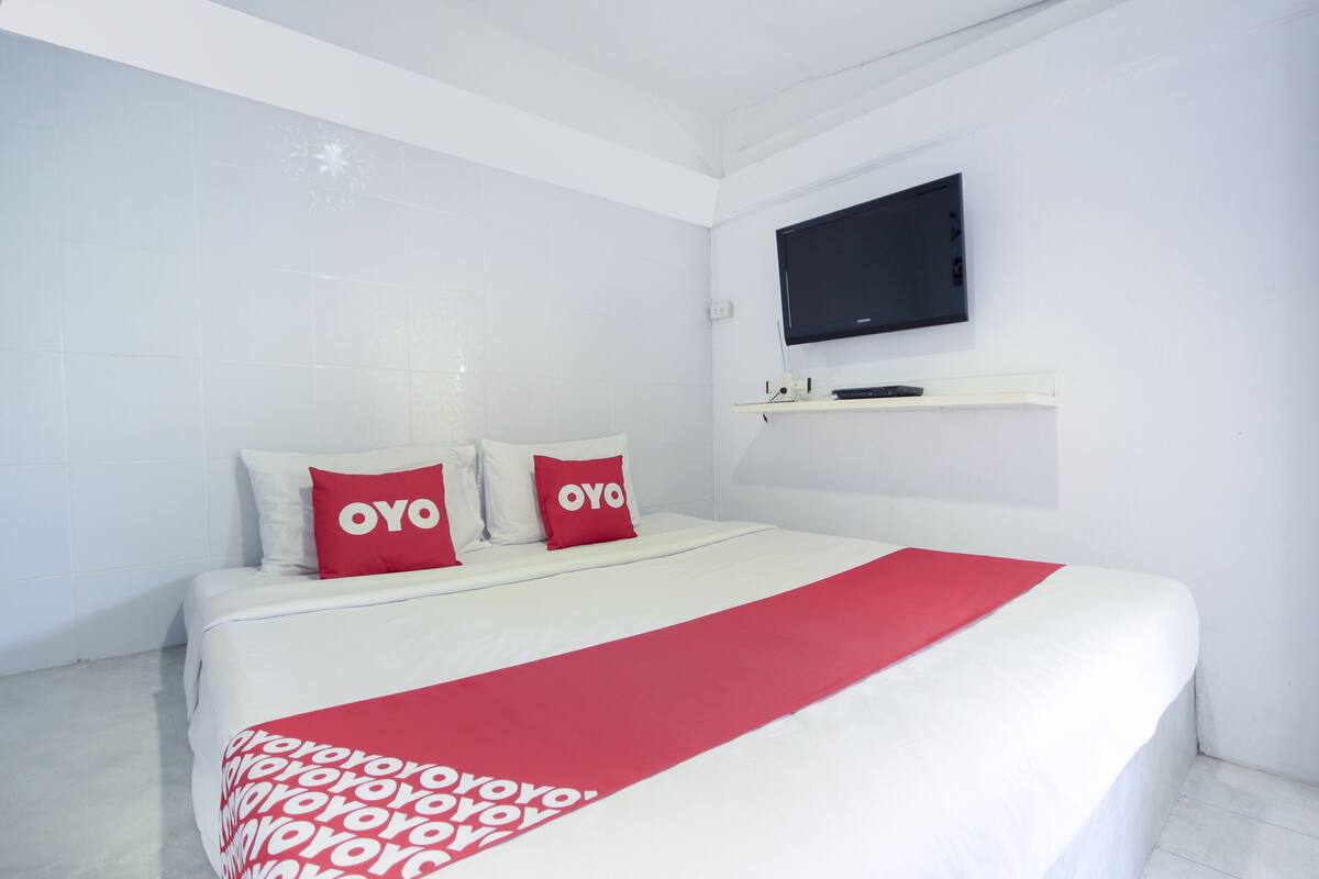A hotel room with a bed, a TV mounted on the wall, and a red and white bedspread.