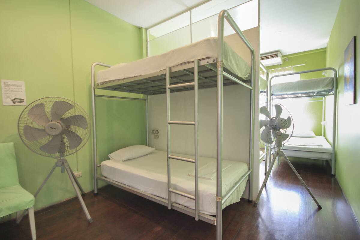 A bunk bed room with a fan, a chair, and a window.