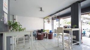 A clean, modern interior with a white tiled floor, a bar area with stools, and a seating area with tables and chairs. - OYO 1054 Phuket Backpacker Hostel (Phuket)
