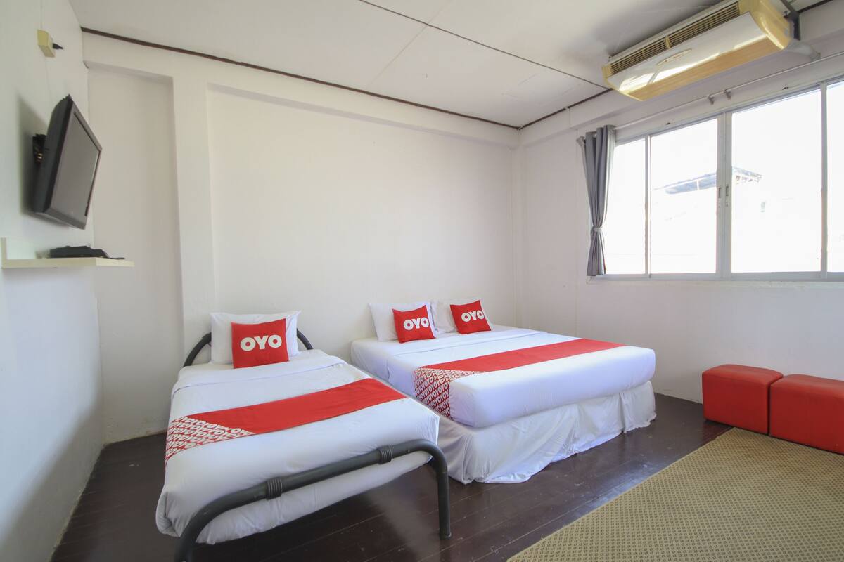 A hotel room with two beds, each with white bedding and red accents, a television on the wall, and a window with curtains.