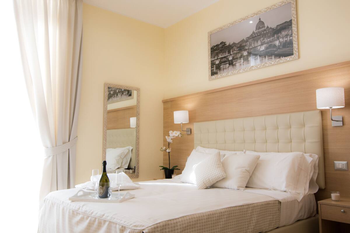 Habitación de hotel con una cama grande, una mesita de noche, una lámpara, un espejo y un cuadro en la pared.