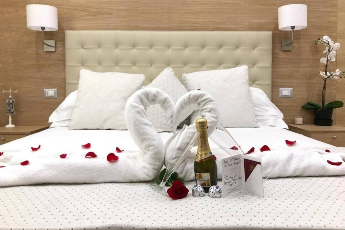 Una cama bien hecha con una toalla con forma de corazón, una botella de champán y pétalos de rosa.