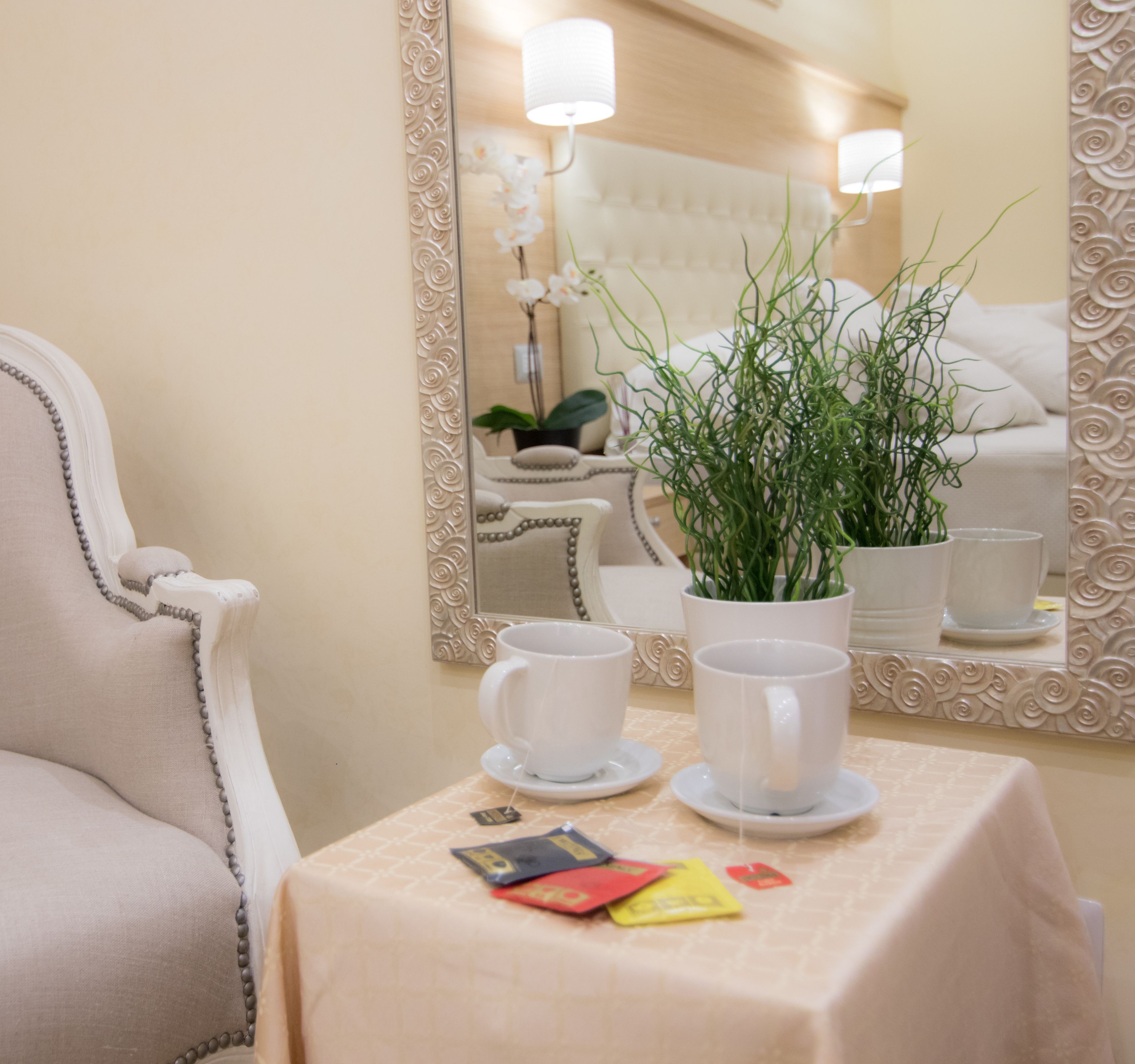 Habitació d'hotel amb un mirall gran, una taula amb estovatge blanc, dues tasses blanques i una planta en test.