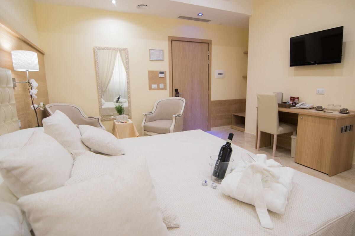 Una habitación de hotel con una cama grande, un escritorio, una silla, un televisor y un espejo.