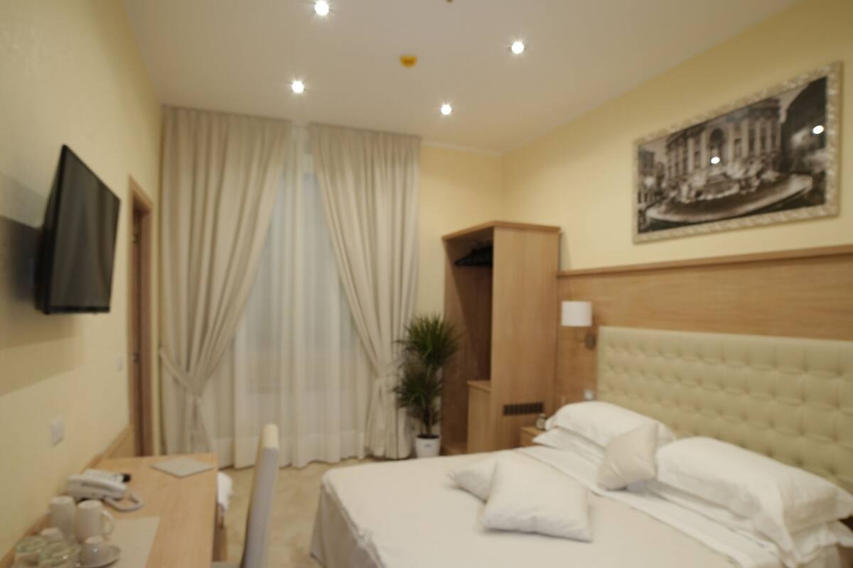 Habitación de hotel con una cama, un escritorio, una silla, un televisor y un cuadro en la pared.