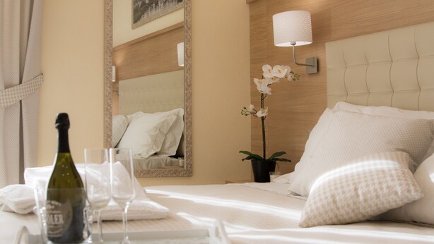 A neatly made bed with white linens, a bedside lamp, and a tray with a bottle and glasses.