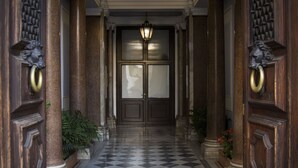 A hallway with a checkered floor, wooden doors with lion head knockers, and a hanging light fixture.