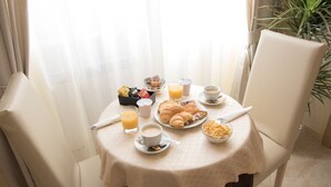 A breakfast table with croissants, a bowl of cereal, a glass of orange juice, and a cup of coffee.