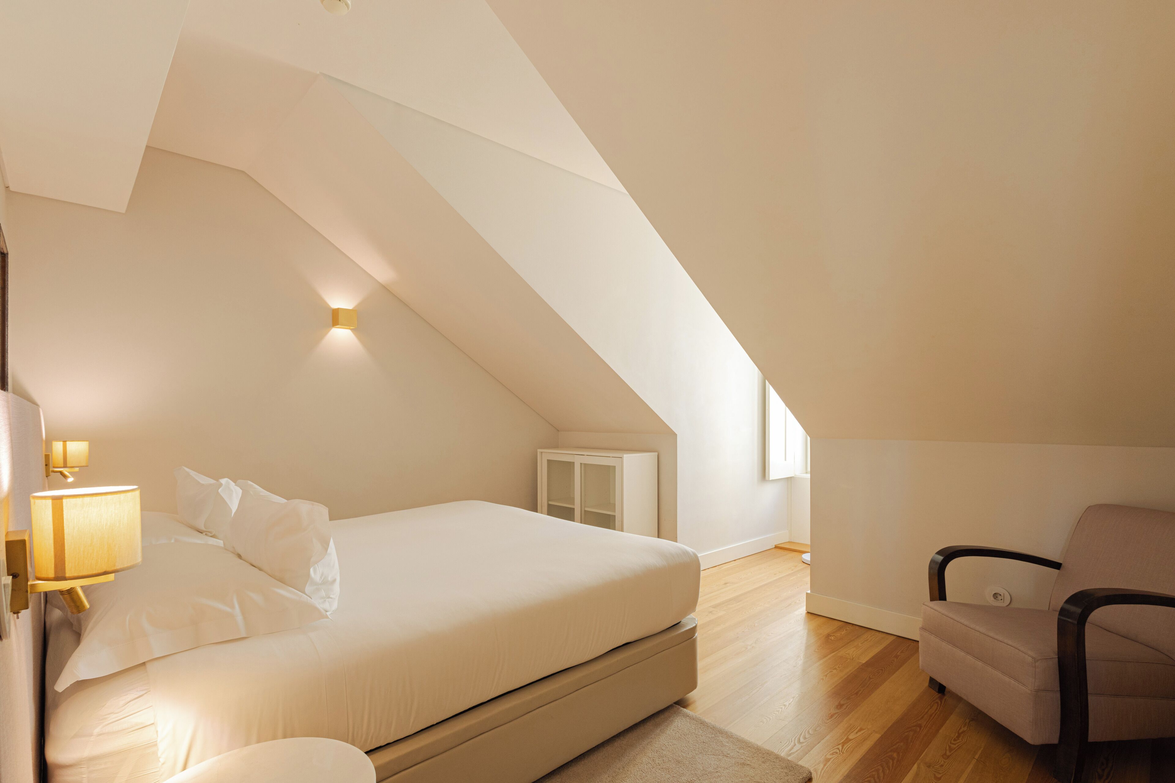 Een slaapkamer met een bed, een stoel, een nachtkastje en een wandlamp.