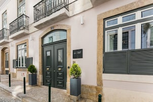 Fachada de edifício com uma porta dupla preta, varanda com grades de ferro forjado e uma placa na parede.