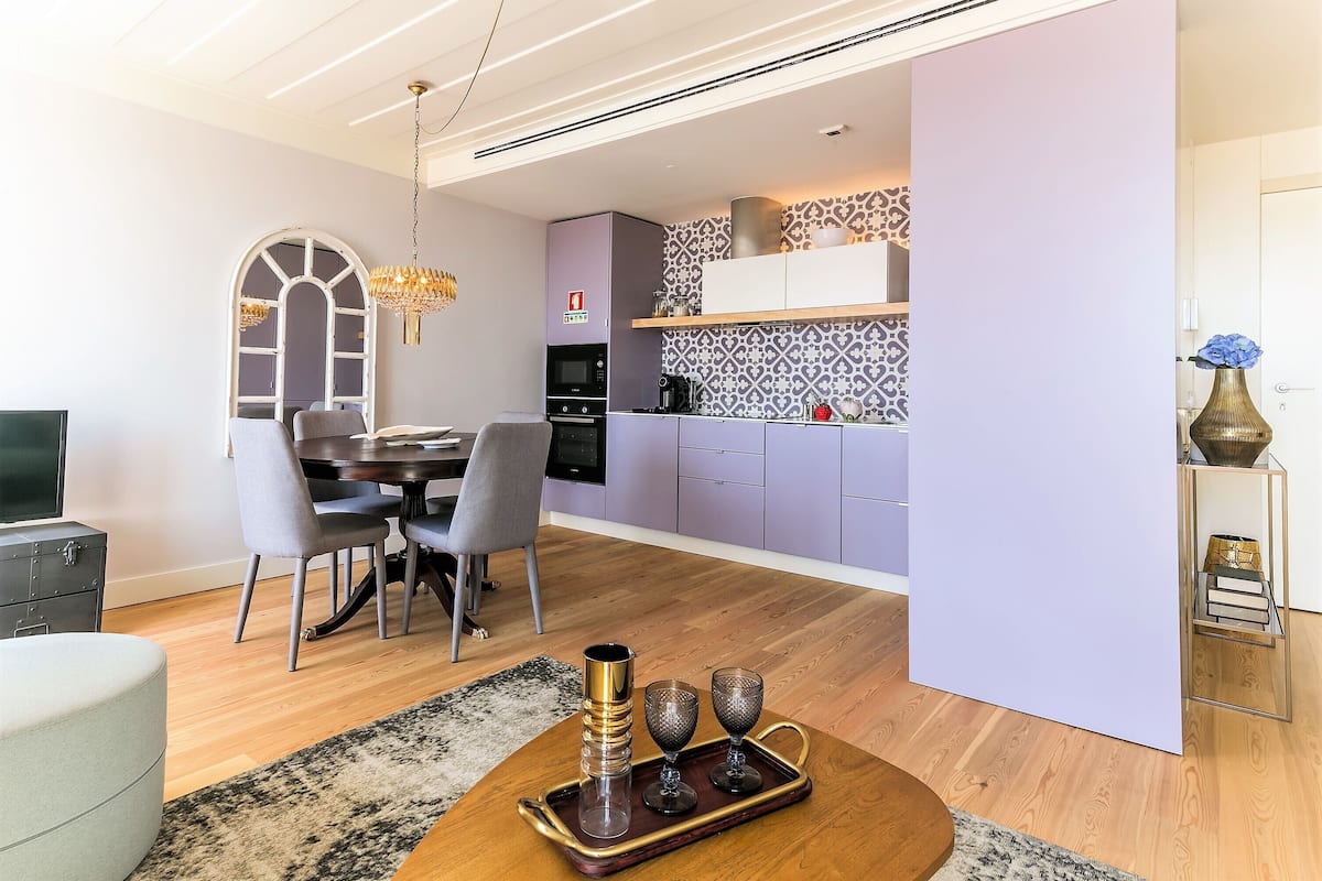 A modern living room with a dining area, a kitchen with purple cabinets, and a large window with a decorative arch.
