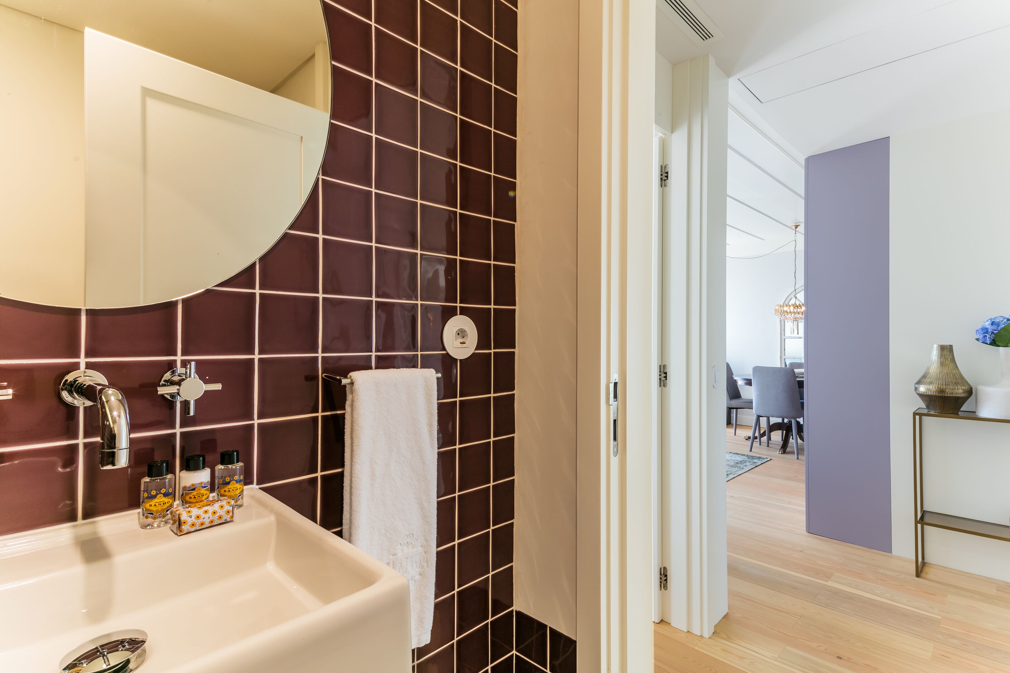 A bathroom with a white sink, dark tiled walls, and a white towel hanging on the wall.