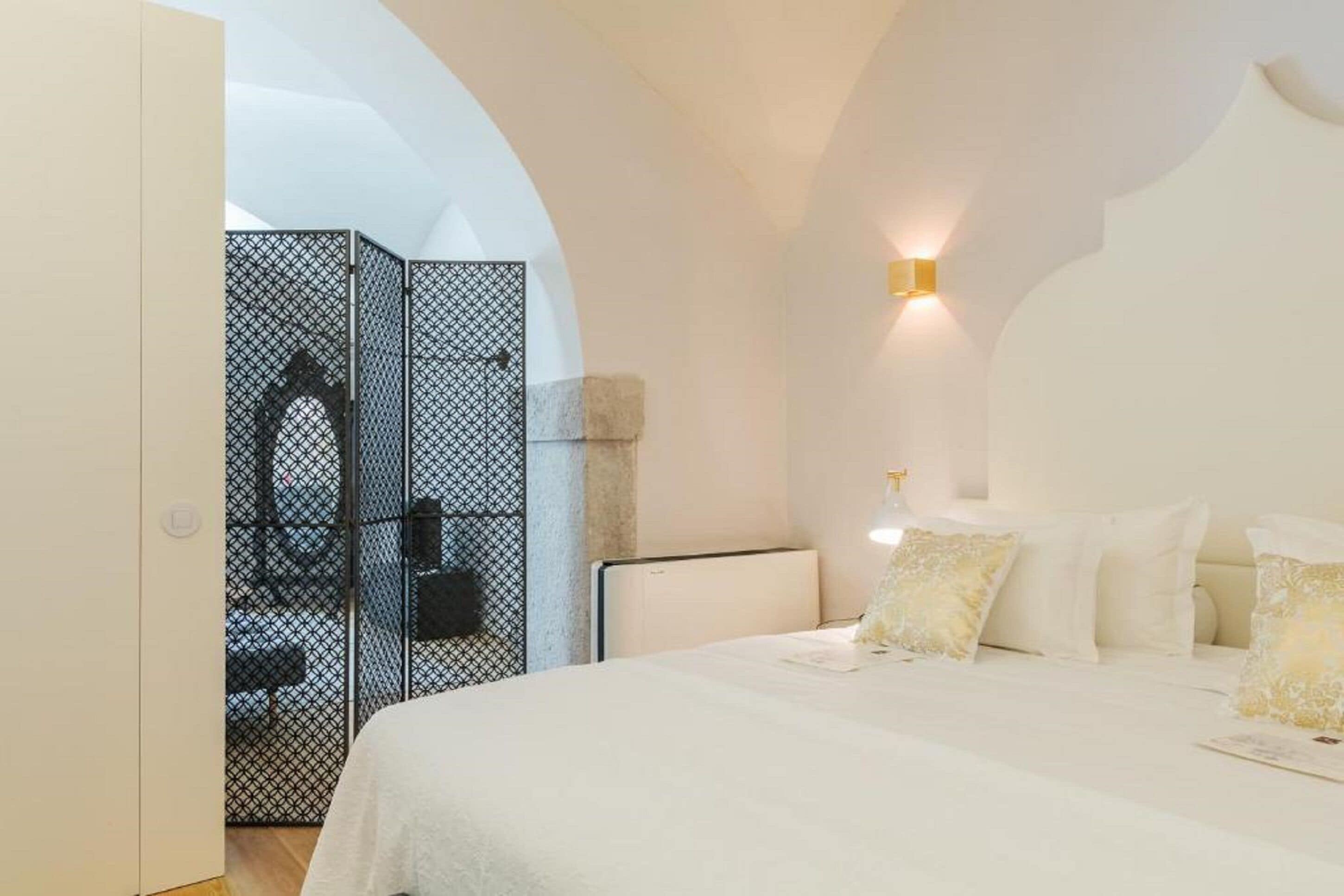 Un dormitorio con una cama grande, cabecera blanca y lámpara de pared.