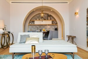 Uma sala de estar moderna com um sofá branco, uma mesa de centro e uma cozinha ao fundo.
