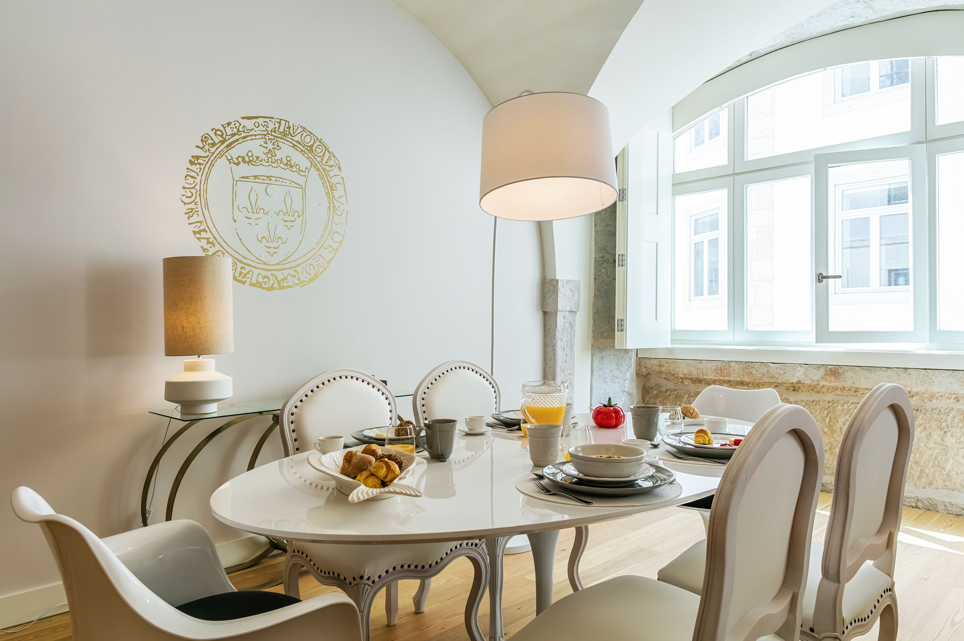 Un coin repas avec une table ronde, des chaises blanches, une lampe et des aliments pour le petit-déjeuner.