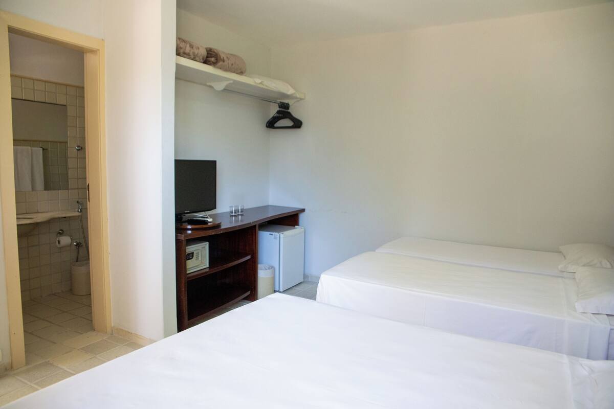 A bedroom with two beds, a small desk with a computer, a shelf with a towel, and a door leading to a bathroom.