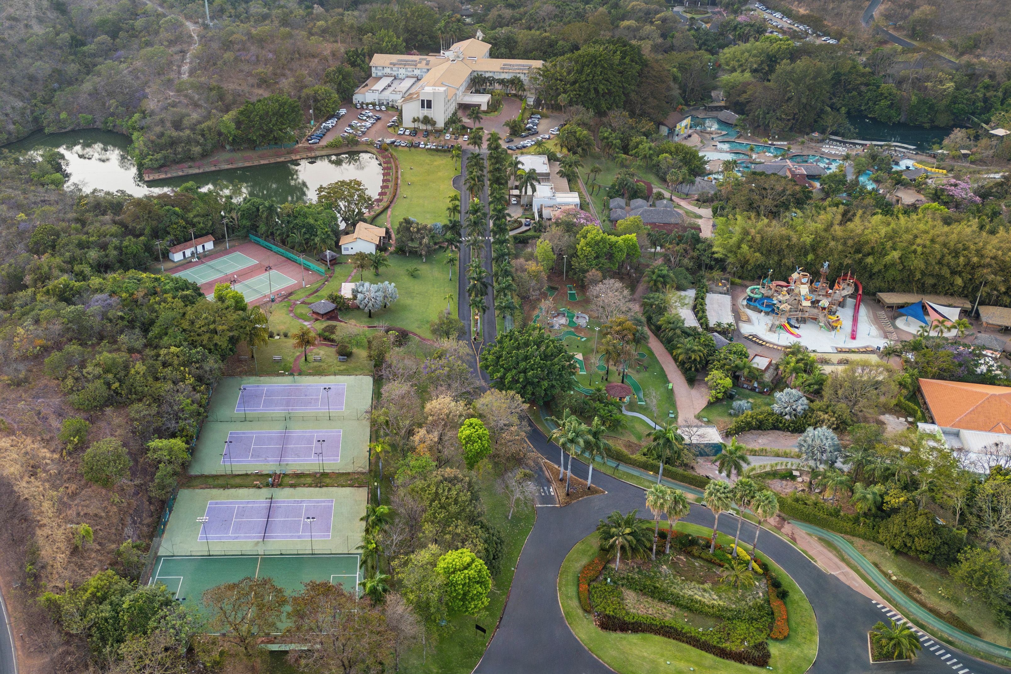 Vista aérea de un complejo turístico con canchas de tenis, una piscina y un edificio grande de varios pisos.