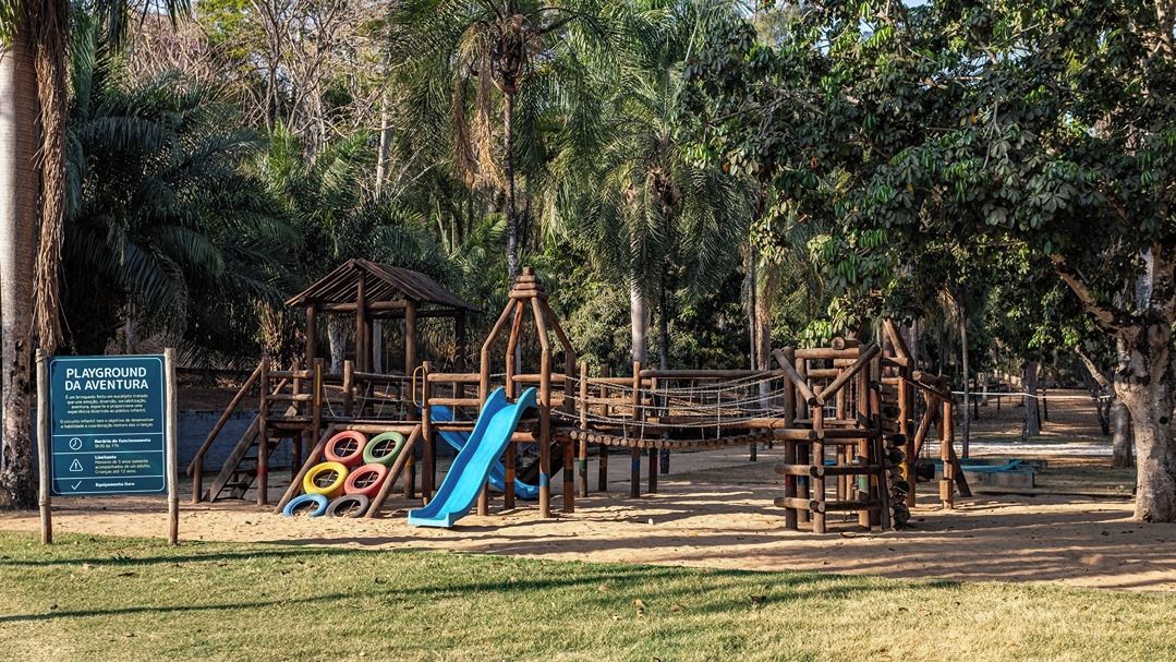 A playground with a slide and climbing structures, surrounded by trees.