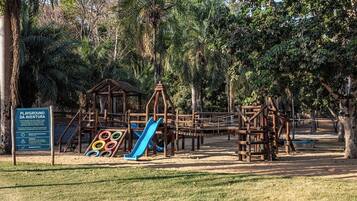 A playground with a slide and climbing structures, surrounded by trees.