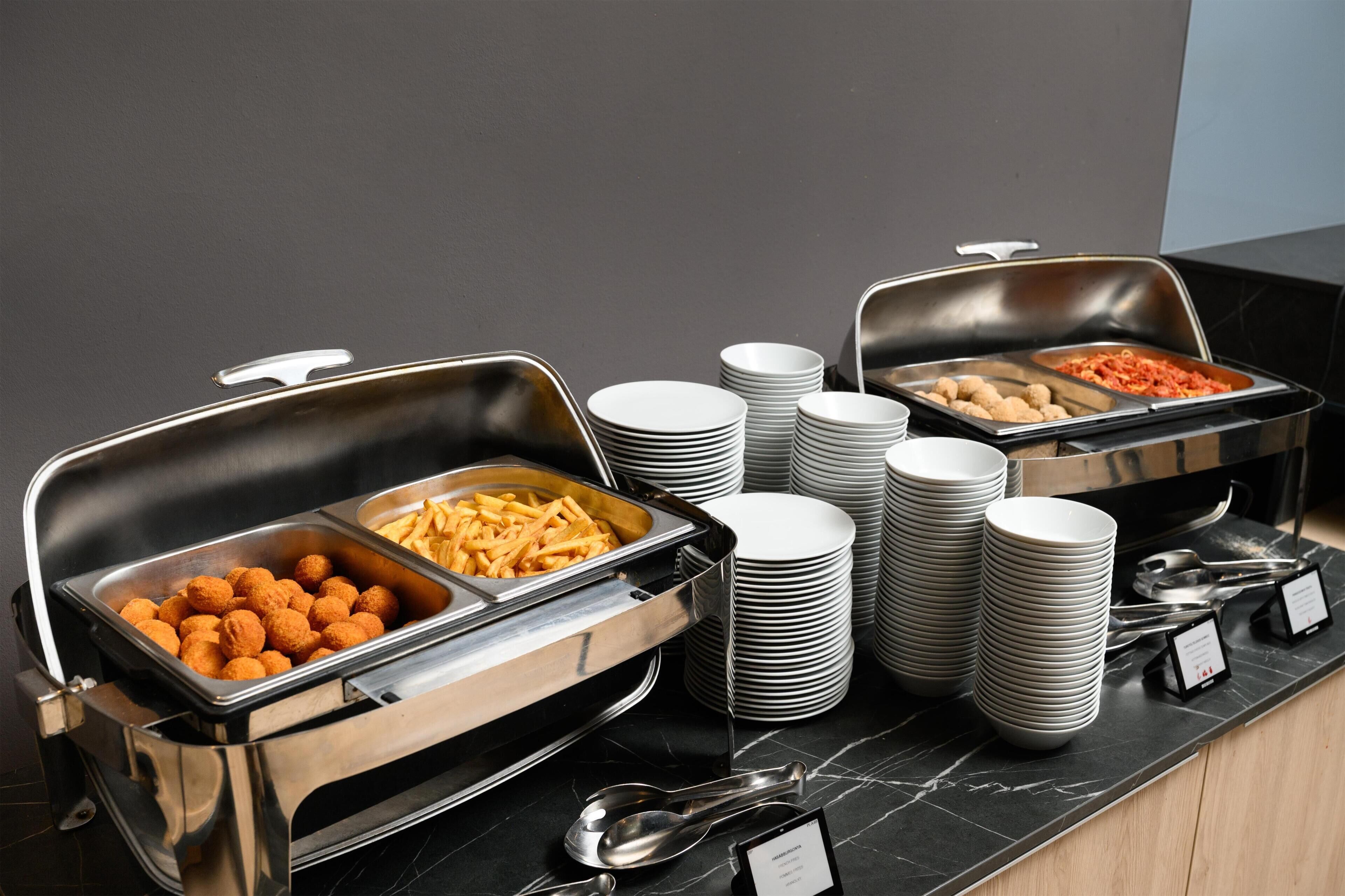 Ein reichhaltiges Buffet mit Speisenplatten, gestapelten Tellern und Geschirr.