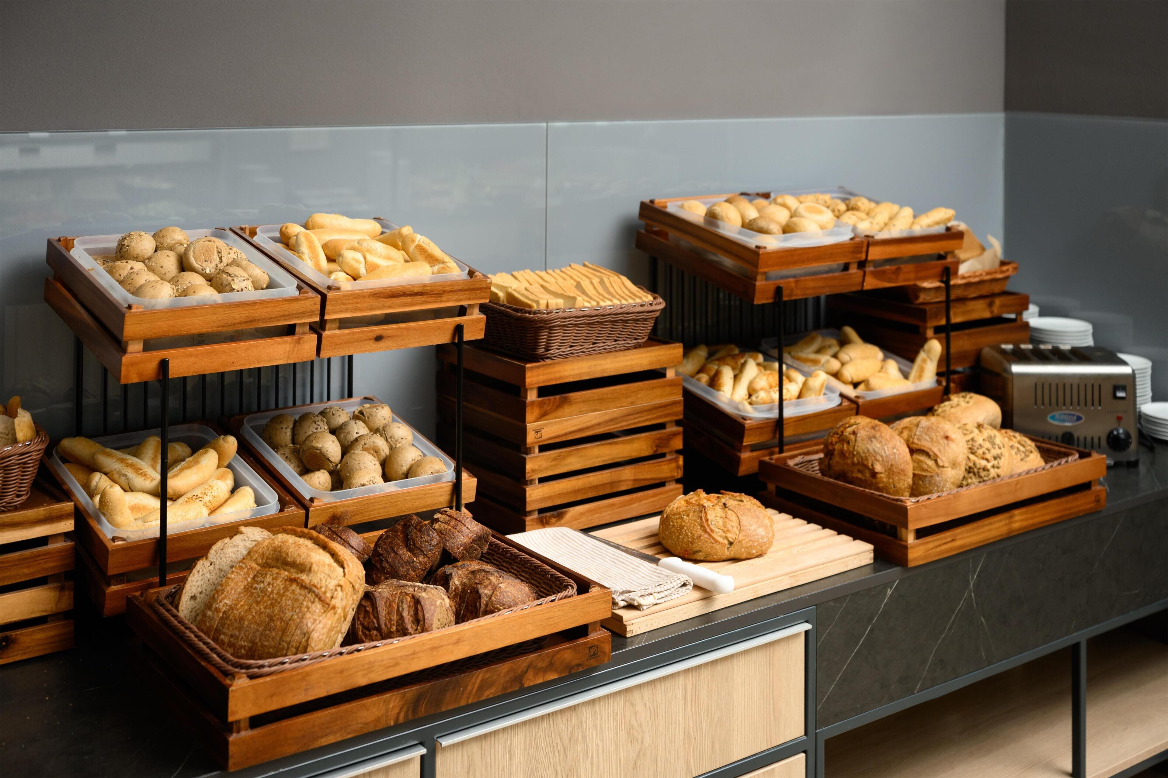A buffet with various breads and pastries in wooden trays.