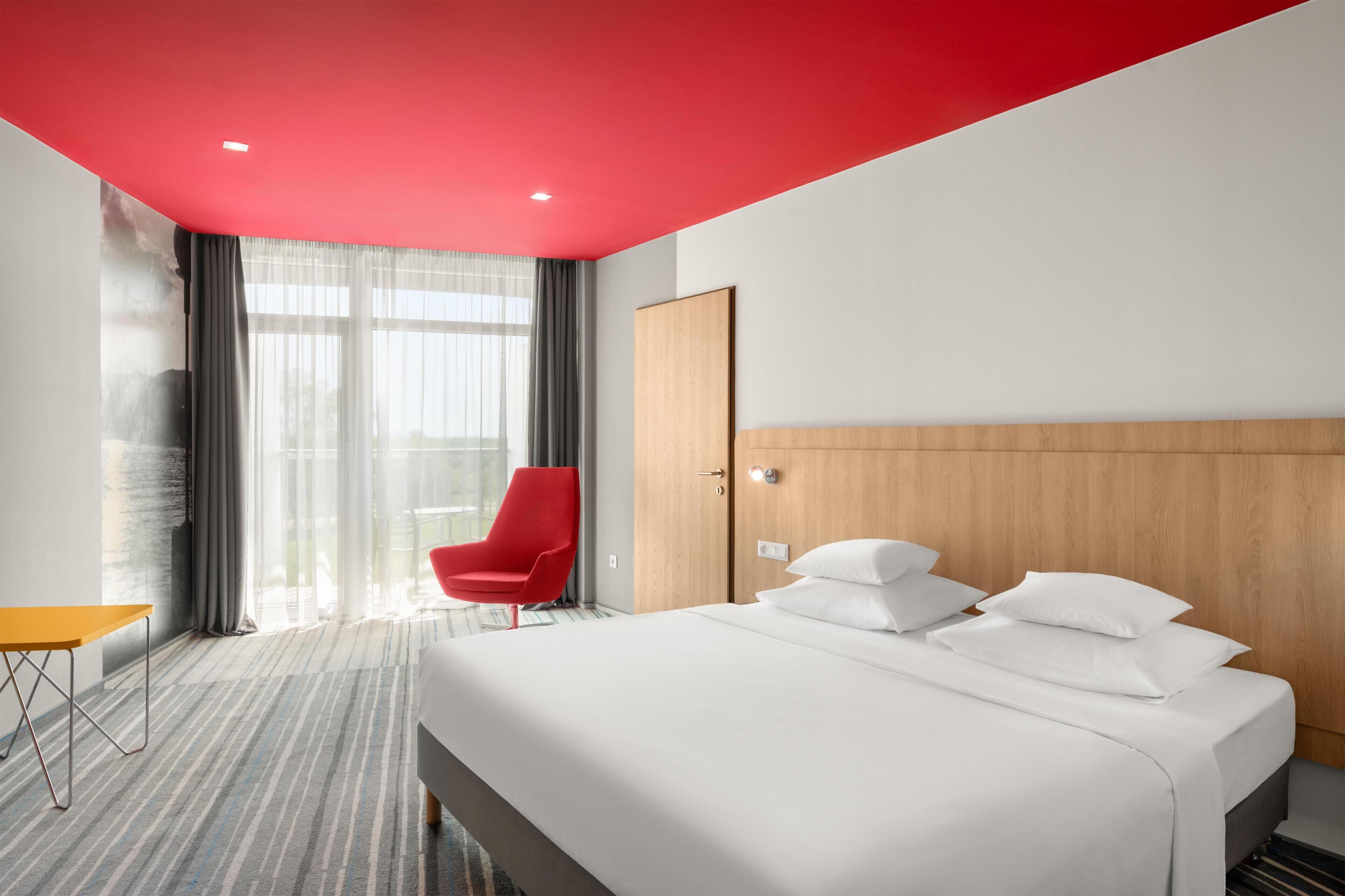 Et hotelværelse med en seng, en rød stol, et træskab og et lille bord.