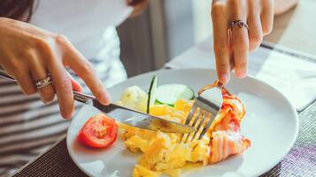 A person eating scrambled eggs with bacon, a tomato, and a cucumber on a plate.