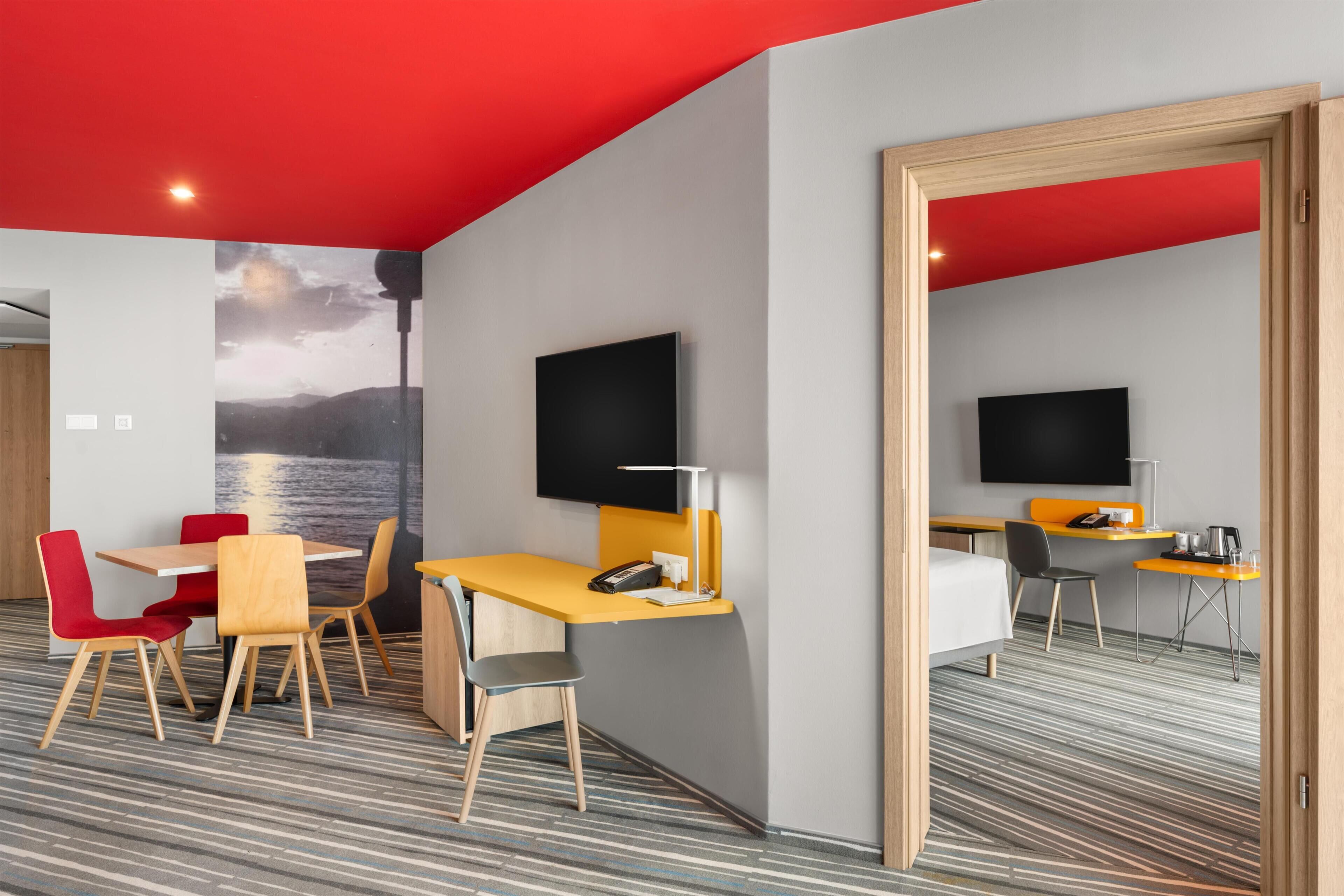 Una habitación de hotel con cama, escritorio, silla, televisor y una ventana grande.