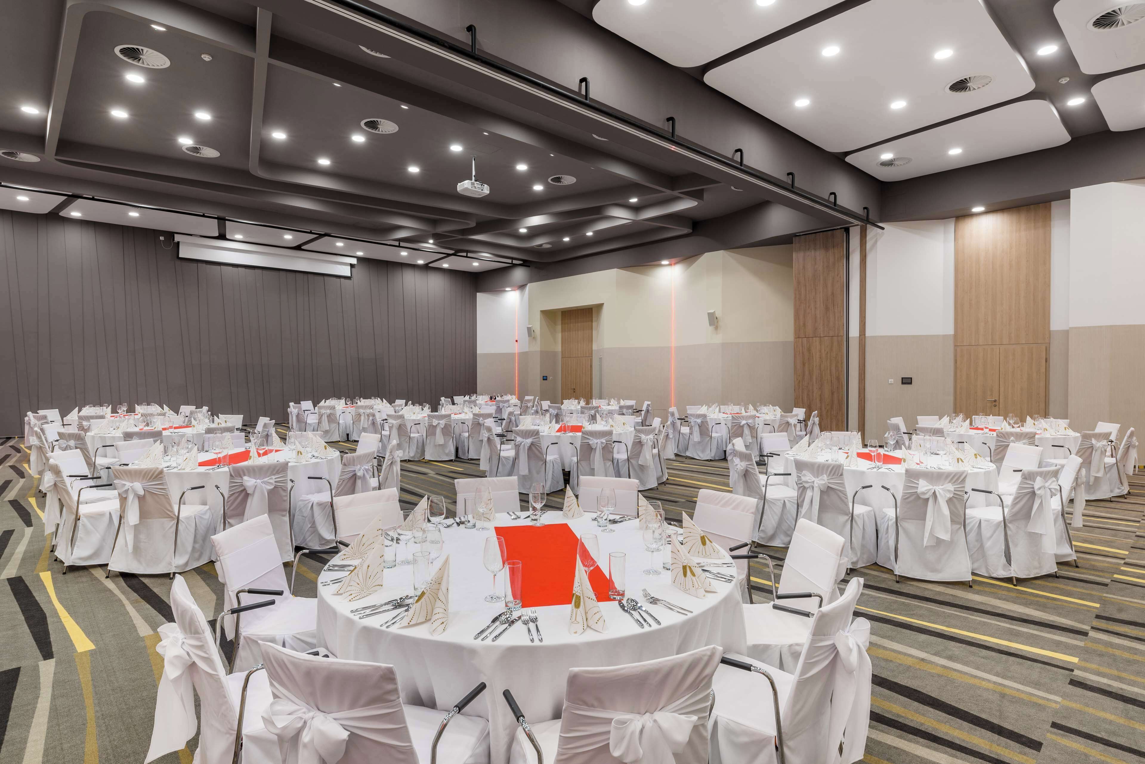 A large conference room with round tables, white chairs, and red table runners.
