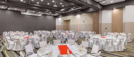 A large conference room with round tables, white chairs, and red table runners.