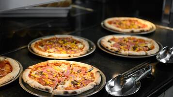 Eine Küchenarbeitsplatte mit mehreren Pizzen auf Metalltellern, einem Metallschöpfkelle und einem Pizzaschneider.