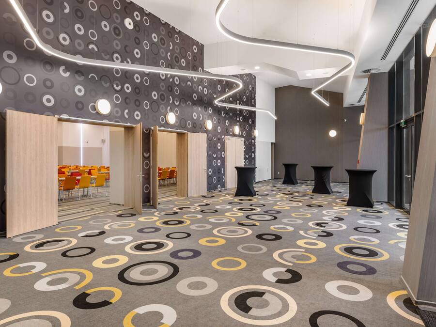 Un interior moderno con alfombra estampada, puertas de madera y un espacio de descanso con sillas naranjas.