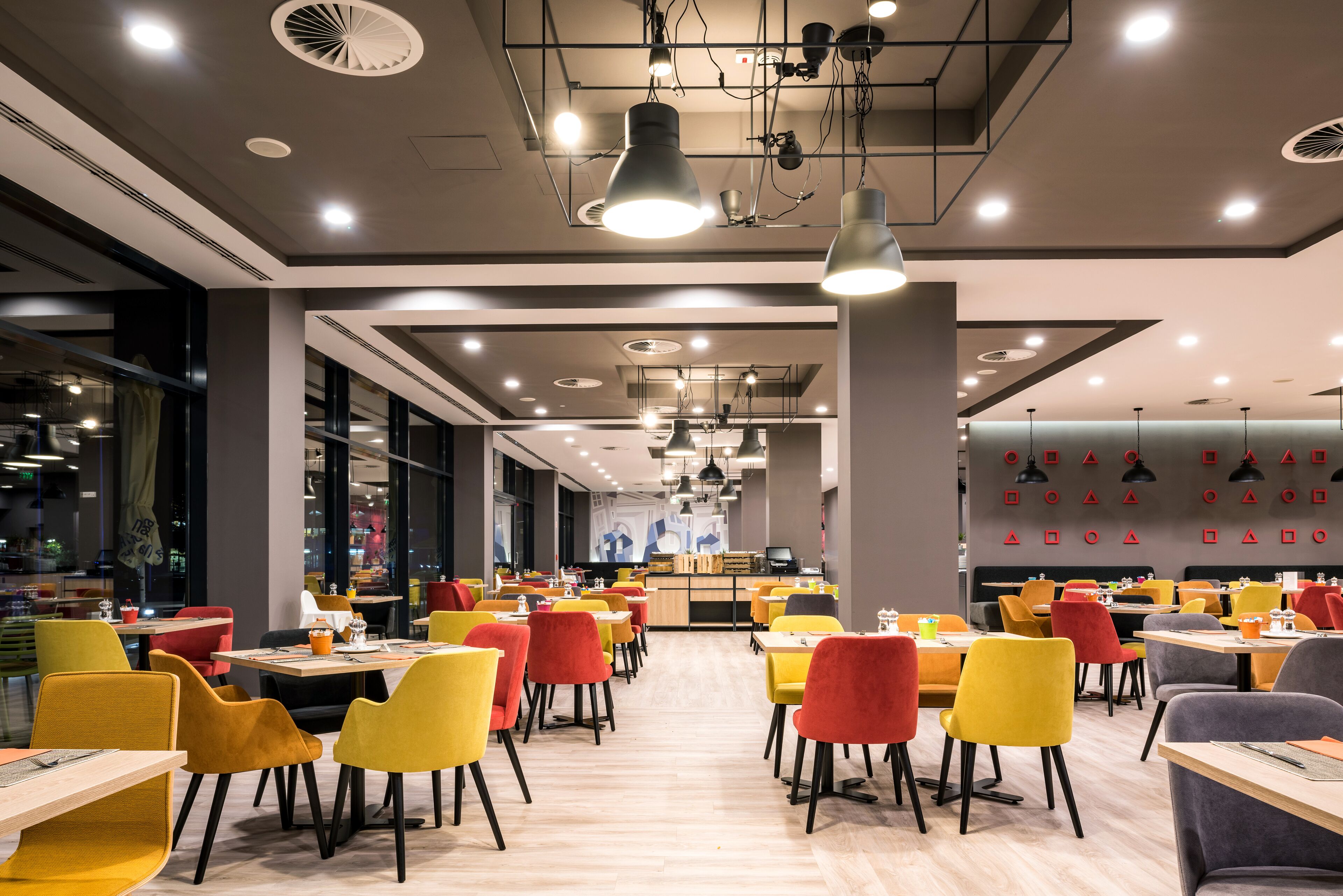 A modern restaurant with multiple dining areas, colorful chairs, and overhead lighting.