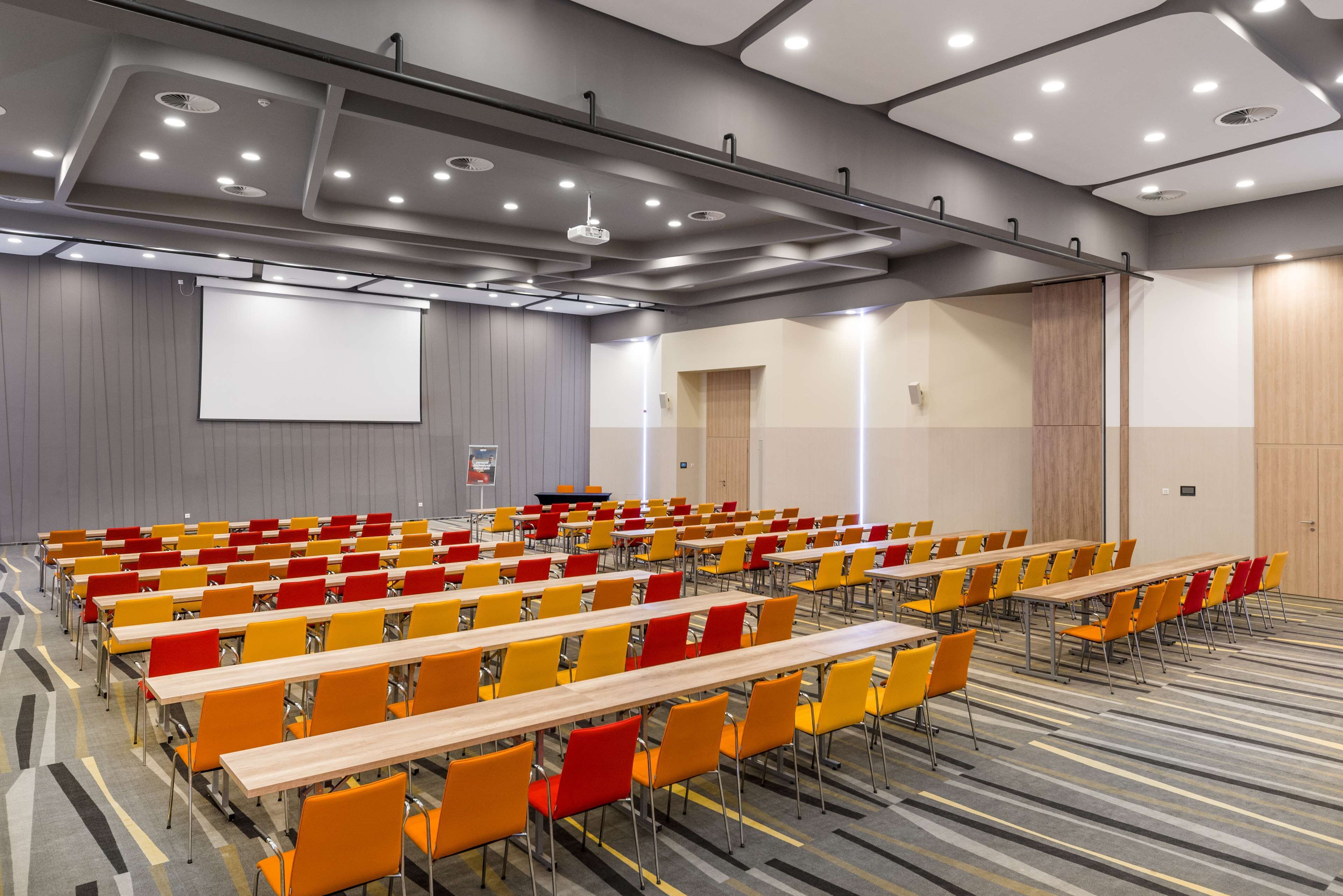 A conference room with rows of tables and chairs, a projector screen, and a podium.