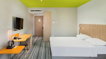 A hotel room with a bed, a desk with a coffee maker, a television, and a door leading to another room.