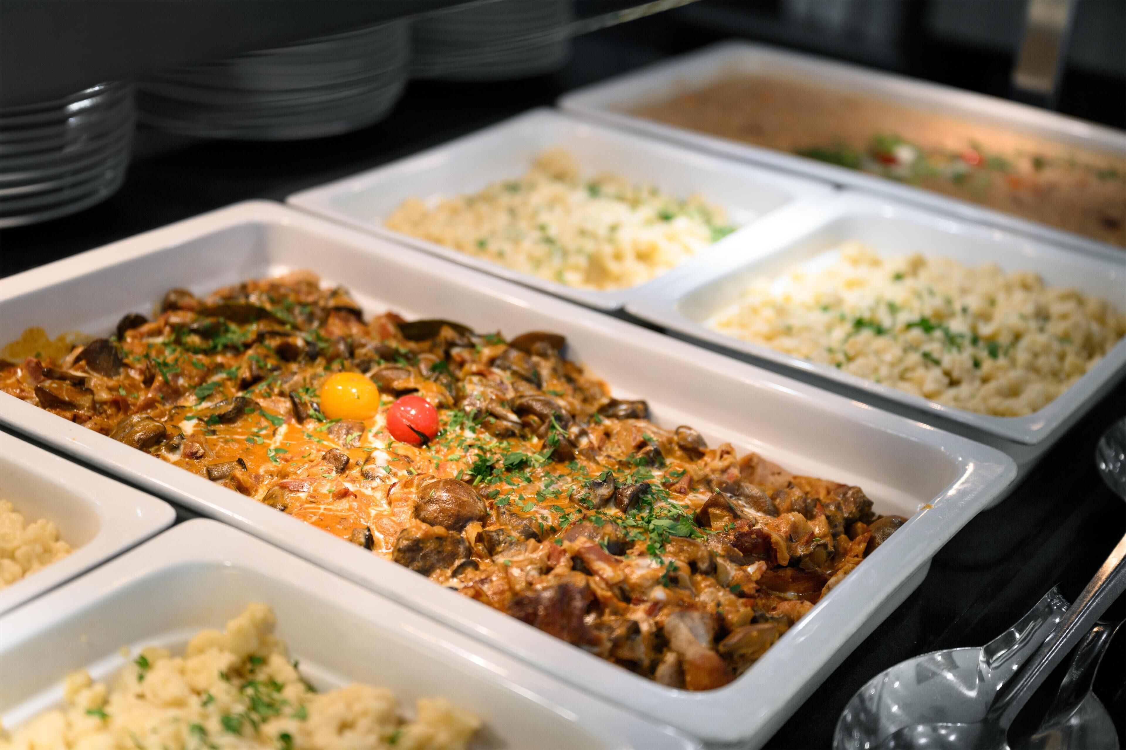 A buffet with various dishes including a meat dish with mushrooms and a tomato garnish.