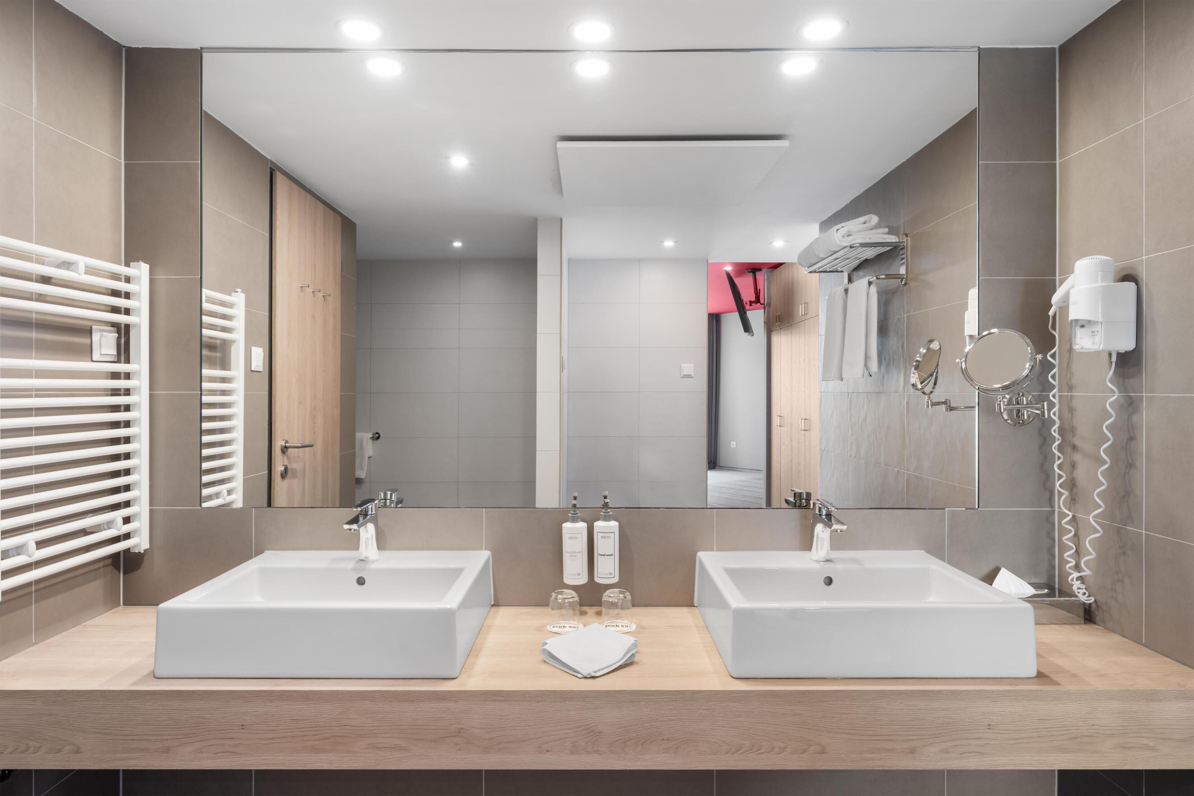 A modern bathroom with two sinks, a large mirror, and a towel rack.