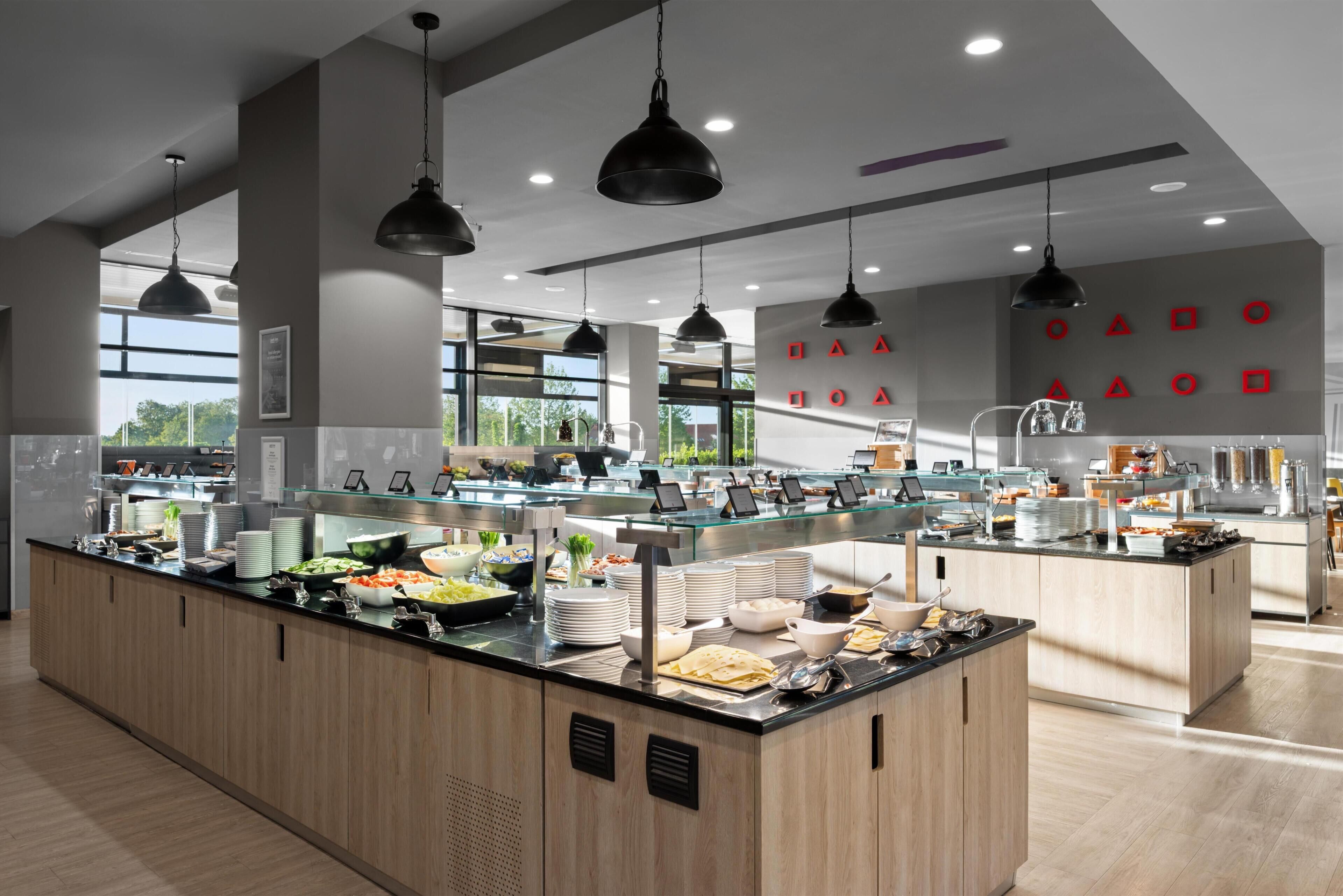A modern buffet with a variety of food items, a large window, and a wall with red geometric shapes.