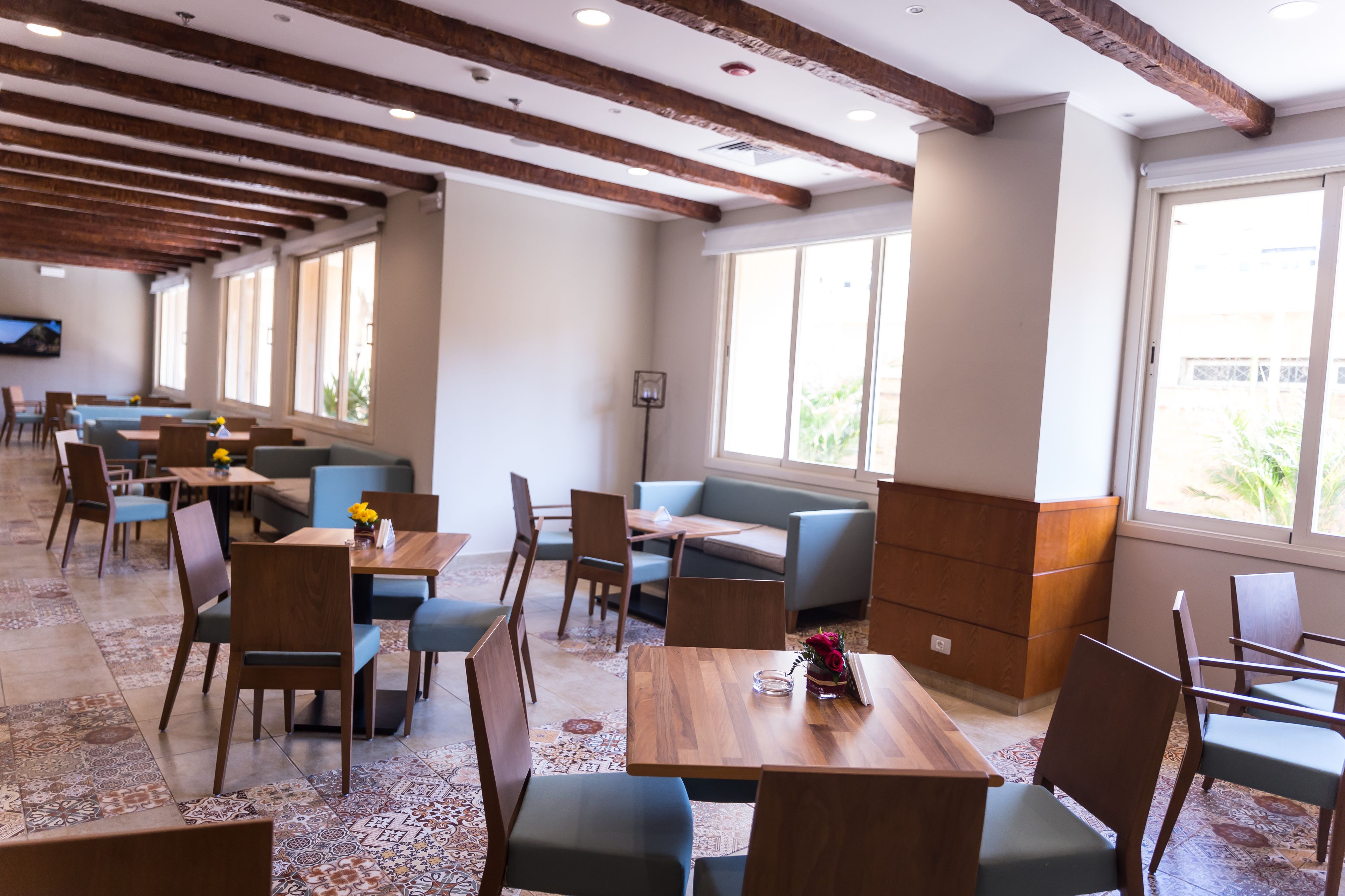 A spacious dining area with wooden tables and chairs, a patterned floor, and large windows allowing natural light.