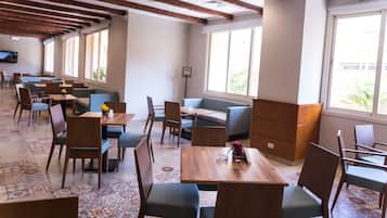 A spacious dining area with wooden tables and chairs, a patterned floor, and large windows allowing natural light.
