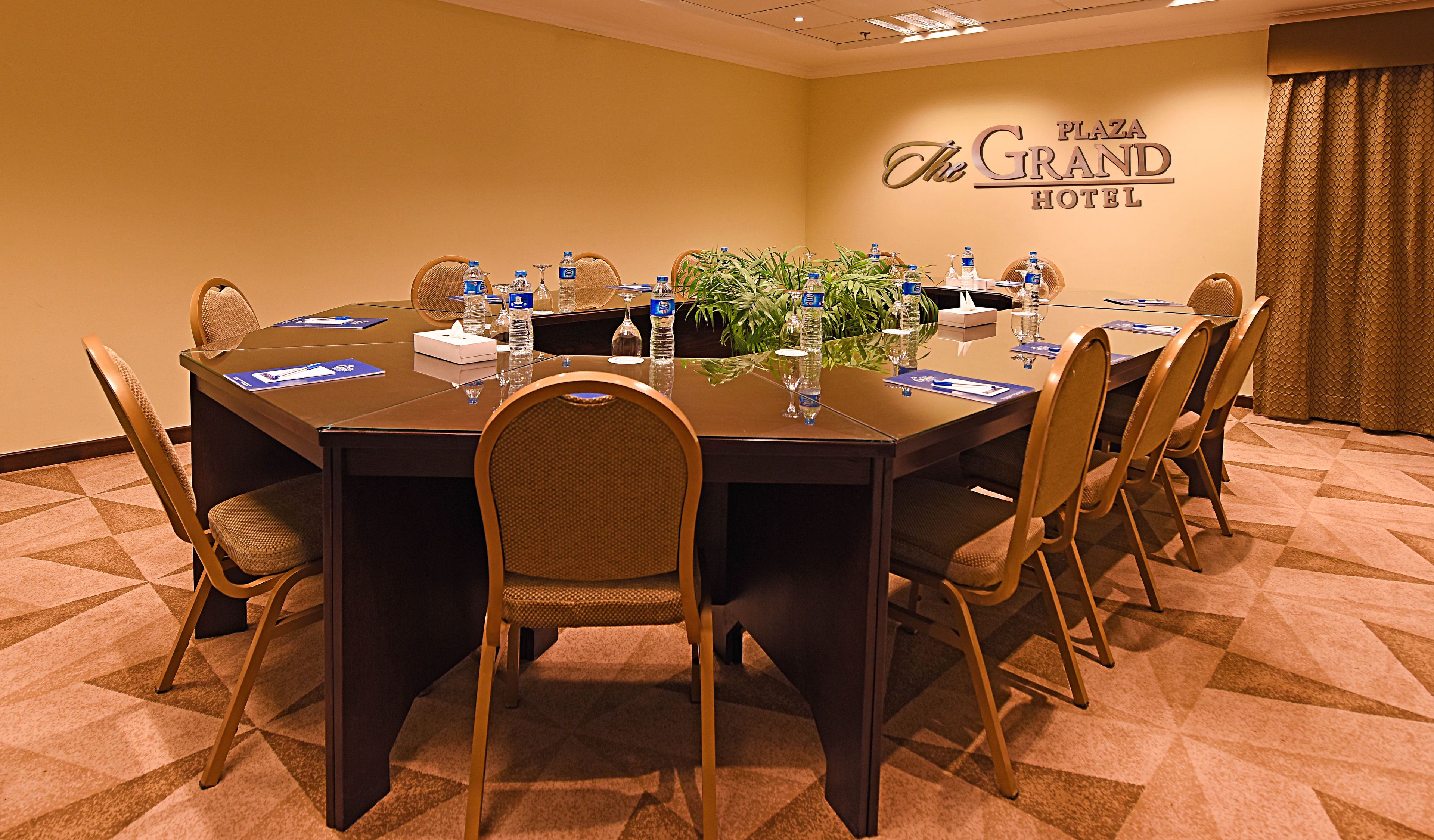 Une salle de conférence avec une longue table, des chaises, des bouteilles d’eau et une plante.