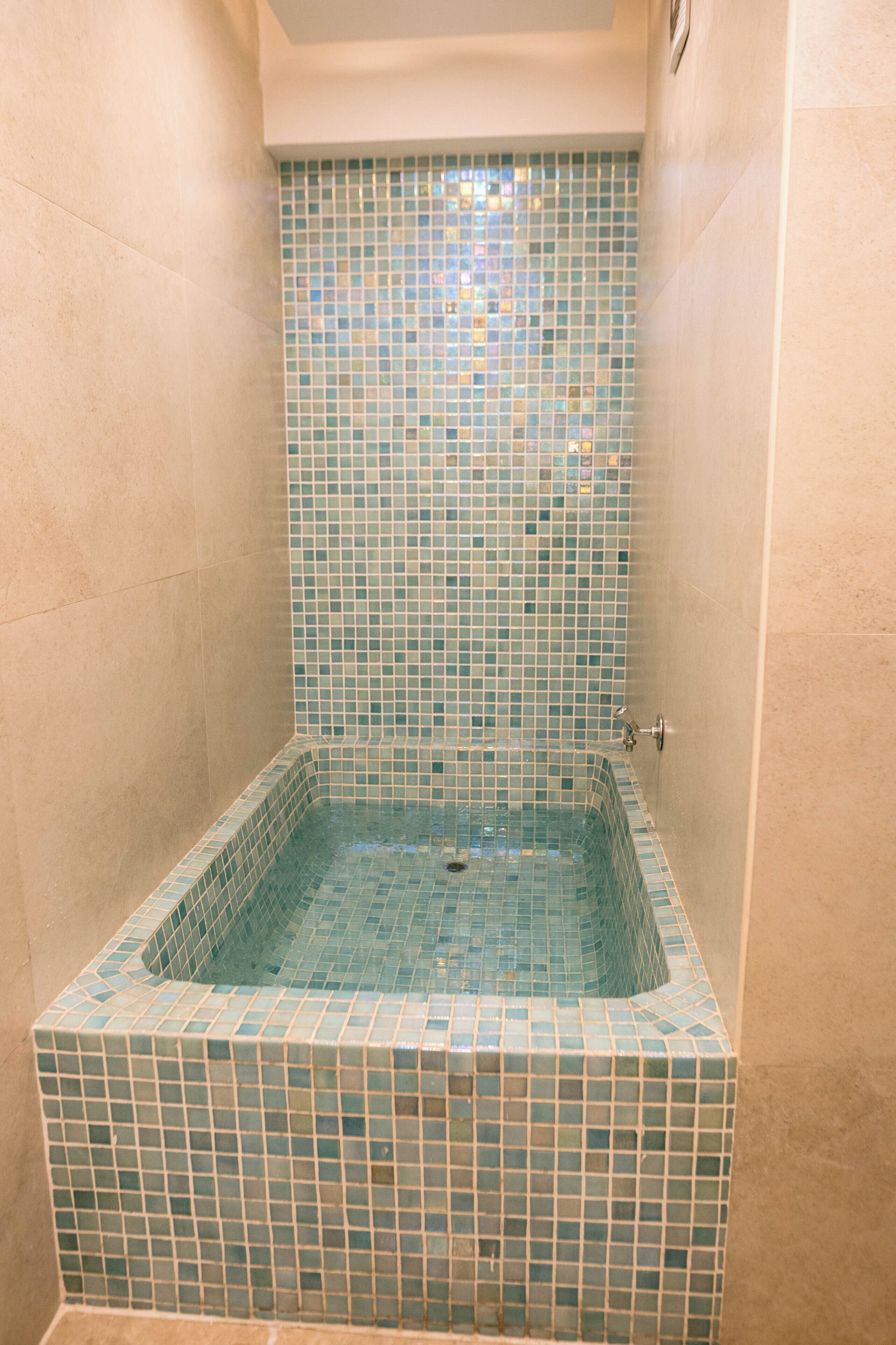 A small, square-shaped bathtub with a tiled interior, surrounded by plain walls.