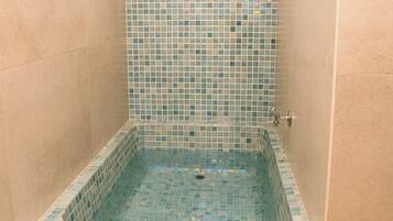 A small, square-shaped bathtub with a tiled interior, surrounded by plain walls.