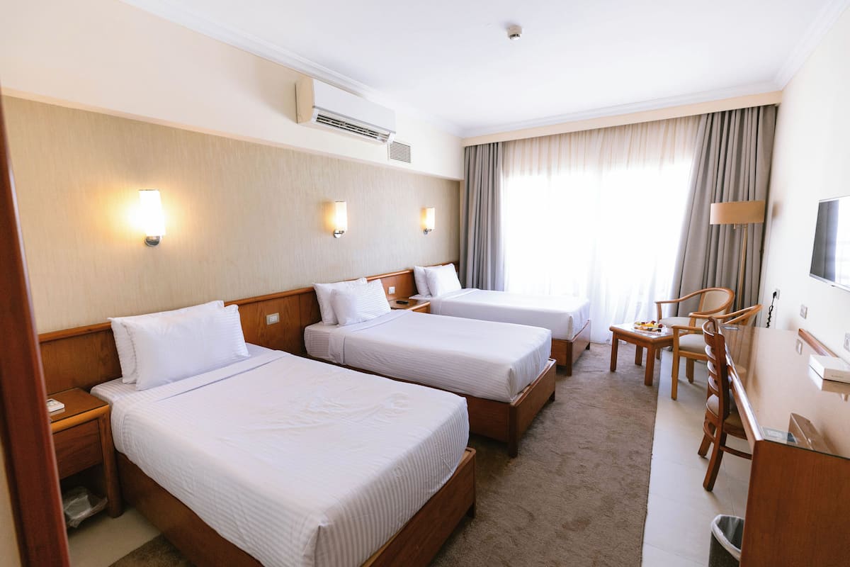 A hotel room with two beds, a desk, a chair, a TV, and a window with curtains.