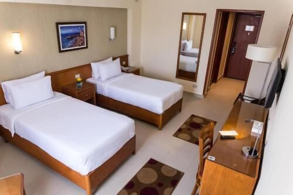 Habitación de hotel con dos camas, un escritorio, una silla, un televisor y un cuadro en la pared.